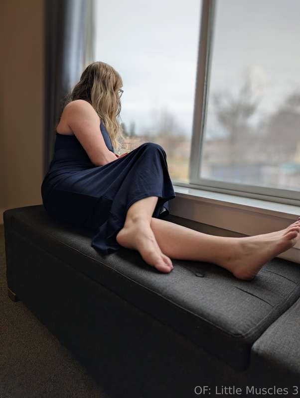 Sunlight warms the glass as she leans against the window, a ..